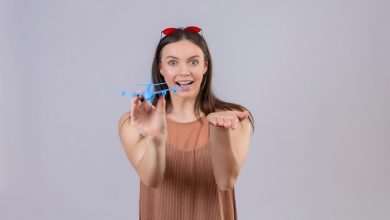 young beautiful woman with red sunglasses head holding toy airplane pointing with arm hand camera smiling with happy face standing white background 141793 24788