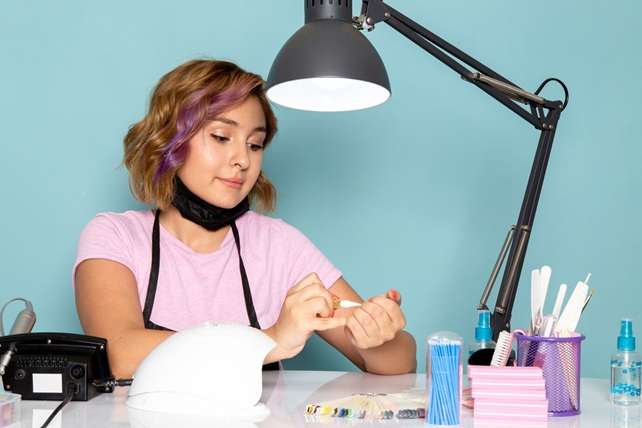 front view young female manicure pink t shirt with black gloves sitting front table working with her nails blue 140725 24253